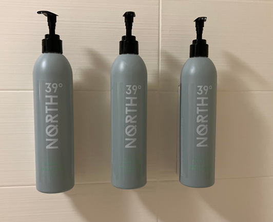 Hotel dispensers for shampoo, conditioner, and body wash. With mint green print on gray bottles, it's nearly impossible to see which is which.