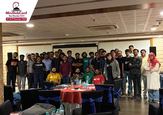 A group of people looking and smiling at the camera. There's various tables, chairs and other conference stuff in view. 