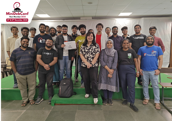 A group of people looking and smiling at the camera. There's various tables, chairs and other conference stuff in view. 