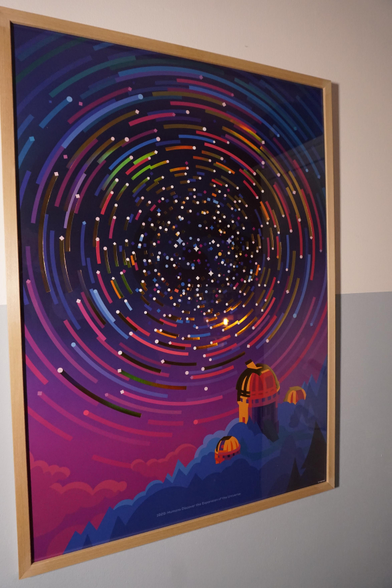 The poster in this photo shows an abstract graphic of a very long exposure photo of the stars at a pole forming rings. In the foreground are observatories too.