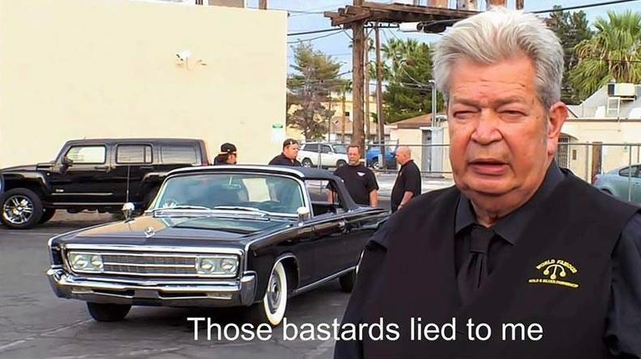 A grey haired man wearing a pawn shop uniform stands in front of a black car. The image is labeled “those bastards lied to me”