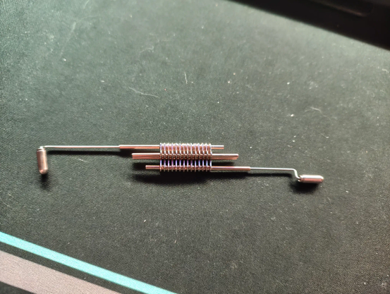 Drei Stäbchen sind mit Spulen verbunden. An der mittleren Spule sind Plättchen angebracht, die sich hochklappen, aber nicht verschieben lassen. 
An den beiden anderen Stäbchen sind dünne, aber sehr feste Drähte angebracht, die am Ende rechtwinklig abstehen. Die Enden der Drähte sind mit einer Kappe versehen, darunter kommt jeweils eine Spitze zum Vorschein. 
