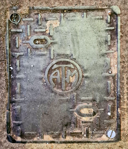 An old cast iron access cover with an Art Nouveau style logo on it.