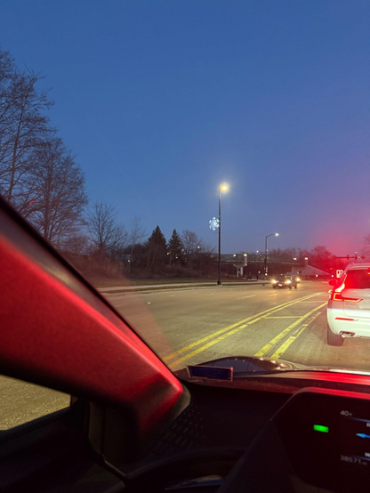 Looking out car window to stopped cars at an intersection in the dark with a snowflake decoration on a light pole