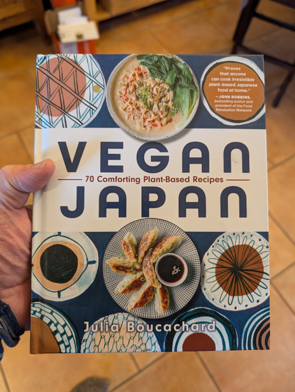 I'm holding a copy of the cookbook Vegan Japan. It's cover has alternating circular graphics, reminiscent of Japanese print art, and plates of food.