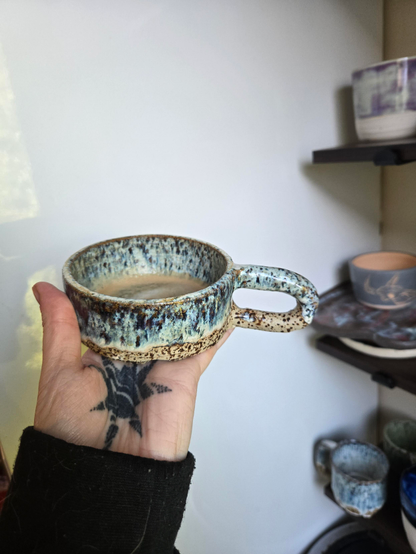 An image of a handmade ceramic mug. The clay is speckled, with a blue and white glaze over top. 