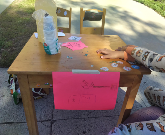 Child sized table with homemade sign selling lemonade.