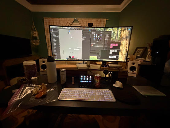 A messy desk with a computer monitor showing apps to set up a stream deck, multiple beverages, and a half eaten slice of cold pizza