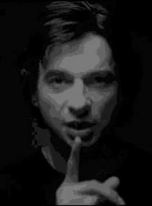 a black and white photo of a man holding his finger to his lips .