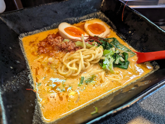 A square bowl of thick miso ramen with greens, spicy minced meat and softboiled egg-halves.