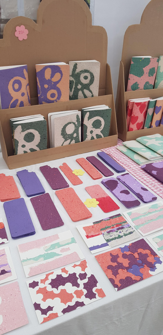 Photo de mon stand lors d'un marché des créateurs en gros plan. Il y a des marque-pages, des carte postales et des carnets en papier recyclé coloré.