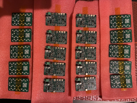 Pictured are 20 PCB's in columns of 5. The first and last columns have the PCB's showing their back with the postmarketOS logo covering it and a QR code for more information, the second and third column are showing the top with all the connectors and transistors and such showing.
The columns are spread out over static-resistance foam layers.