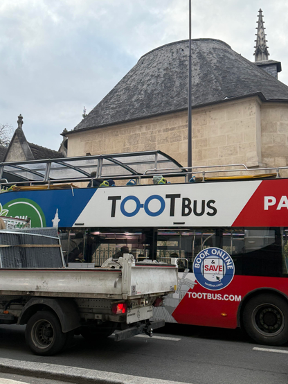 A French bus with the words “toot bus” on it in front of a beautiful old building. They just don’t make old buildings in the US like they do in Europe 