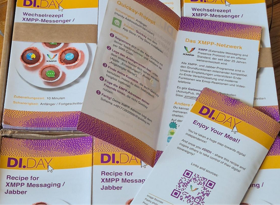 Mehrere gedruckte Faltblätter und Karten zum Thema **XMPP/Jabber** liegen aufgefächert in einer Schachtel. Überschriften wie „Wechselrezept XMPP-Messenger“, „Recipe for XMPP Messaging“ und „Enjoy Your Meal!“; farbiges Design (Gelb/Lila), Icons, kurze Erklärtexte und ein QR-Code. Foto: GeOrG (vermutlich cc by)