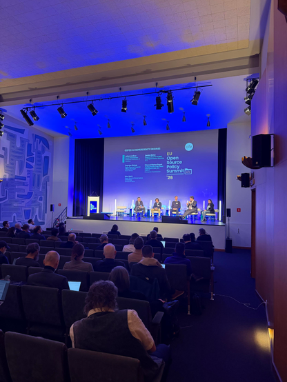 Several panelists sitting on stage at the EU Open Source Policy summit, with many people sitting in the audience.