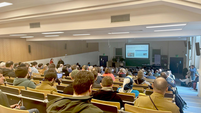 View from the back of a crowded lecture hall during the "Funding the FOSS Ecosystem" Devroom at FOSDEM