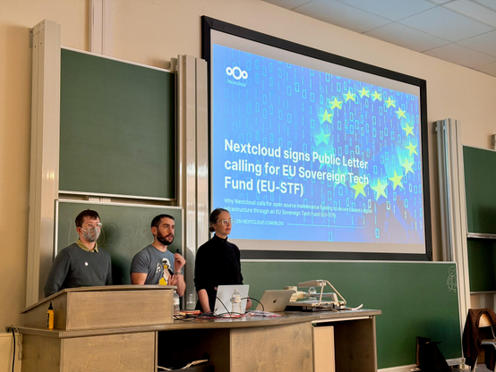 Photo of the presenters during the "Funding Europe’s Open Digital Infrastructure: A Detailed Case for an EU Sovereign Tech Fund" session with Nicholas Gates, Felix Reda, Jennifer Tridgell. The slide being projected on the screen reads, "Nextcloud signs Public Letten calling for EU Sovereign Tech Fund (EU-STF)"