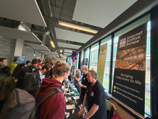 Two men interact with the public at the Internet Archive Europe stand at FOSDEM in Brussels