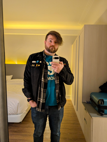 Cassidy wearing a GNOME shirt, black and gray flannel, and black denim jacket with a bunch of pins