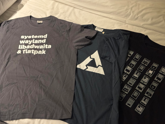 A picture of three T-shirts. One systemd/libadwaita, one postmarketOS and one Proxmox.