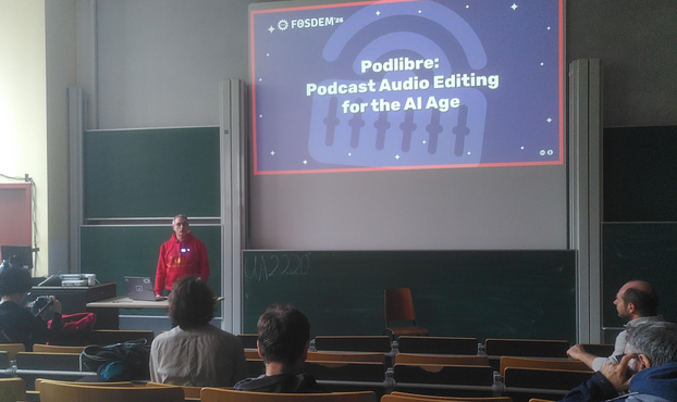 FOSDEM stage with the presenter and the title slide of the talk stating: Podlibre: Podcast Audio Editing for the AI Age
