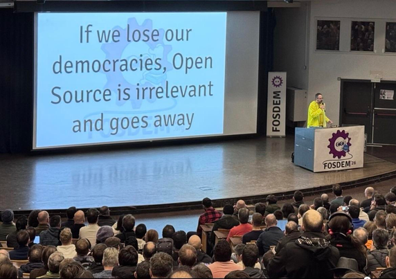 A full auditorium top level view of the stage and screen that says in large letters “If we lose our democracies, Open Source is irrelevant and goes away”