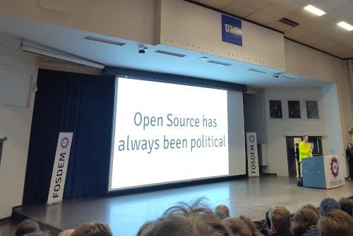 A photo of a projection screen in an auditorium with the words "Open Source has always been political".
