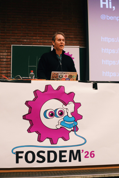 a photo of Ben Pate on stage at FOSDEM speaking during his presentation