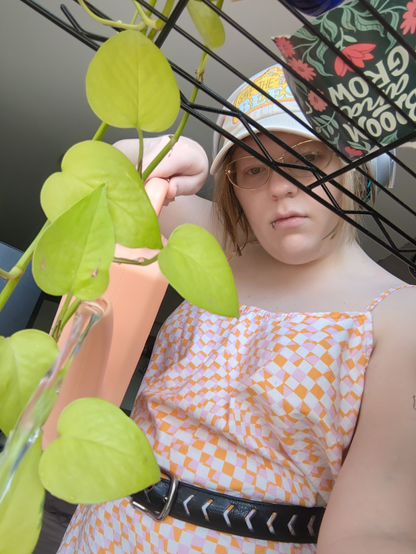 Many, obscured by a shelf as you sit among the plants, waters you while wearing a VERY cute pink&orange-checkerboarded-with-white dress, with a belt around the middle, and a baseball cap that says "save the bees" in orange!