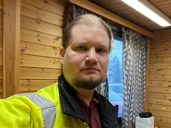 A selfie-style picture of me, a Nordic looking guy with a beard, wearing a high-visibility jacket over a business casual outfit. An office with wood paneling walls can be seen in the background.