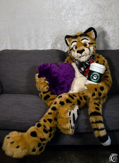 In fursuit sitting on a sofa holding a fuzzy purple heart and giant cup of coffee