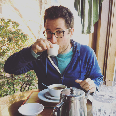 A photo of Jason sitting at a restaurant and sipping a cup of tea. In front of him is a bowl of soup and a tea kettle.