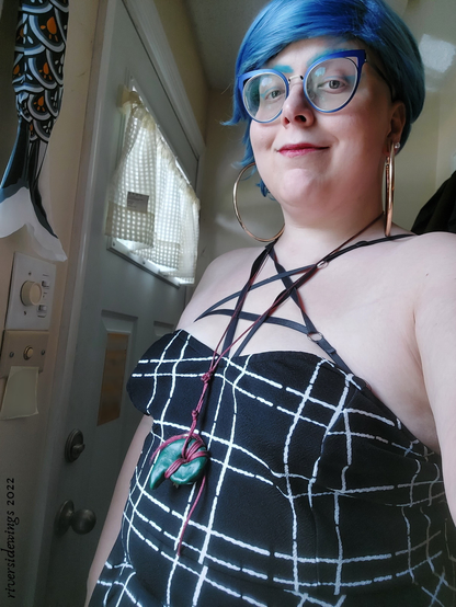 A blue haired Armenian dyke in a pentagram harness and strapless dress.