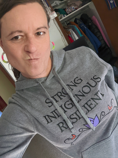 It's uncomfortable to describe what I look like. I'm wearing brightly coloured beaded hoop earrings and a grey hoodie with the bold words underlined by floral artwork: STRONG, INDIGENOUS, RESILIENT
