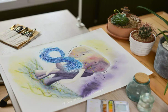 Vue d’atelier de l’œuvre “Gardien de la Mémoire du Vivant”, aquarelle  et mix media. Elle représente un éléphant majestueux qui marche sur un tapis d'herbes, de fleurs et de lignes géométriques rappelant la structure de l'ADN. De sa trompe sort un jet d'eau en forme d'infini. Au dessus de sa tête un ciel violet et jaune et des oiseaux stylisés noirs. Elle est posée sur une table entourée de pinceaux et de plantes, en lumière naturelle.