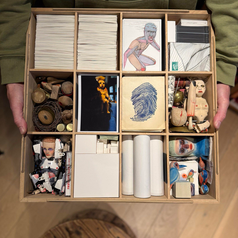 Un boîte séparé en douze compartiments dans lesquels sont ranger des dessins, des sculptures.