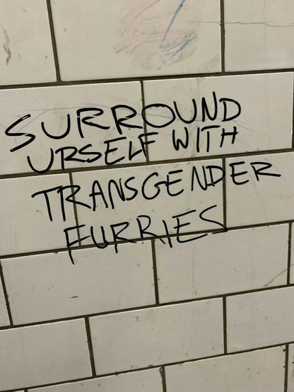 Graffiti on a tiled wall "SURROUND YOURSELF WITH TRANSGENDER FURRIES"