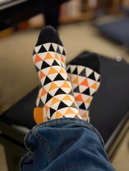 bunt gemusterte socken mit orange und schwarzen dreiecken, die wie das peerTube-Logo aussehen.