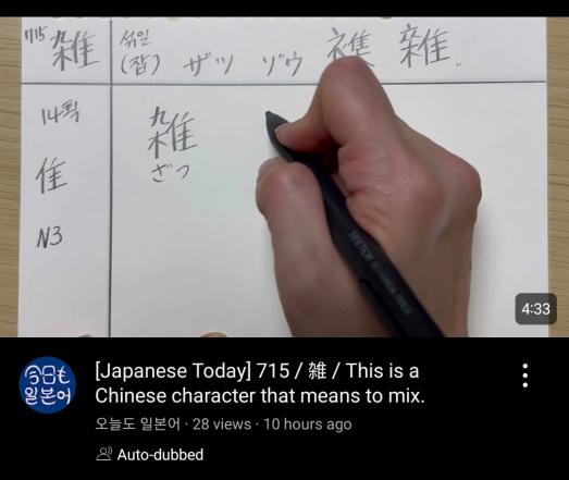 Hand practices writing Japanese Kanji on paper with a pen. The paper displays the character 雜 and its reading "zatsu," along with annotations in Korean and Katakana. Below the video frame, text reads: "[Japanese Today] 715 / 雜 / This is a Chinese character that means to mix." and the channel name "오늘도 일본어."