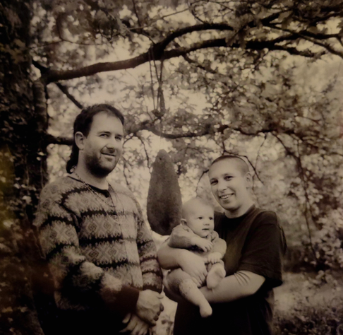 Photo argentique sépia de deux adultes et un bébé sous un arbre au printemps.