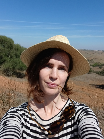 Selfie of speaker, a white brunette woman, outdoors and wearing a straw hat.