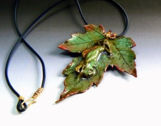Handcrafted polymer clay maple leaf with warm copper edges, featuring a woodland tree nymph sleeping on the leaf. The nature-inspired necklace has a 14kt bail with sparking garnets and hangs from a black buna cord with hand crafted 14kt clasp. It evokes a quiet forest floor after rain.