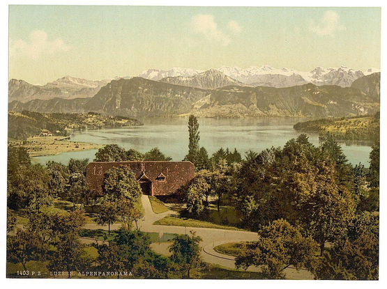 The image displays a picturesque landscape featuring lush greenery, with a large body of water reflecting the blue sky and distant mountains. A traditional building with dark roofing stands prominently in the foreground on what appears to be well-maintained grounds surrounded by trees, shrubs, and manicured gardens. The structure has an arched entrance adorned with numbers '13' above it, suggesting historical significance or a commemorative purpose.

In the background, majestic mountains rise against a clear sky, their peaks hinting at snow-capped elevations that contribute to the scene's serene beauty. Nestled among these natural features is what looks like a town or village on the far side of the water body, adding a touch of human presence without detracting from the landscape's overall tranquility.

The vintage aesthetic of the image suggests it may be an old postcard depicting Lucerne and its environs in Switzerland during late 19th to early 20th century. The colors are muted with sepia tones dominating, giving a nostalgic feel that evokes memories of past travels or romanticism associated with travel photography from this era.

The text at the bottom indicates "LUZERN." ALPENPANORAMA," which translates to "Lucerne Alps panorama" in English and refers to Lucerne's Alpine scenery. The postcard number, 1403 P.Z., is likely a reference used for cataloging or identifying [...]