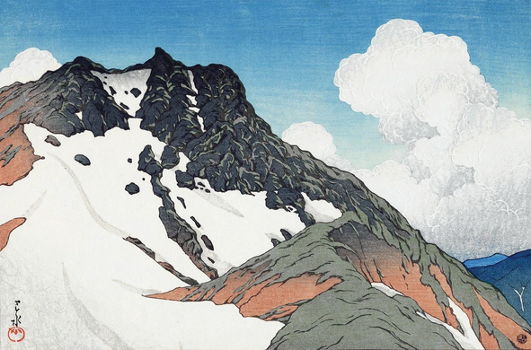 A view looking out over the Hida mountains on a bright day in Nagano, Japan. Slowly melting snow is retreating between ridges on rugged mountain terrain; bare earth, green grass and dark rock are showing through the snow. The sky above is blue, the horizon populated by stacks of tall white clouds.