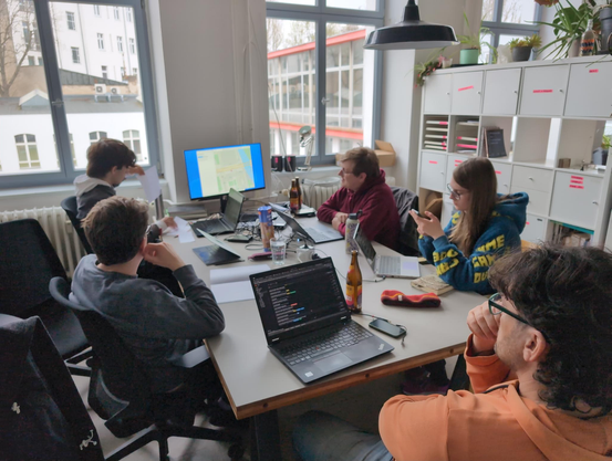5 hackers sitting around a table looking at a monitor with an maps app together.