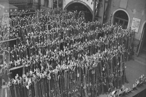 A black and white image of several racks filled with skis in a train station hall.