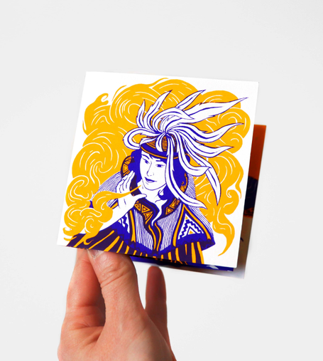 Cette photo montre une main tenant un petit leporello imprimé en sérigraphie. Sur la couverture, on peut voir une illustration en deux couleurs, jaune et violet, qui représente une femme portant une coiffe composée de longues plumes ondulantes. Son visage est tourné vers la gauche. Elle tient sa main et soufie dedans, faisant sortir de ses doigts une fumée orange. Ses vêtements sont ornés de motifs graphiques évoquant le tissu brodé. L’édition est photographiée sur fond blanc. Ce leporello fait partie d’une série sérigraphiée, disponible sur ma boutique en ligne.