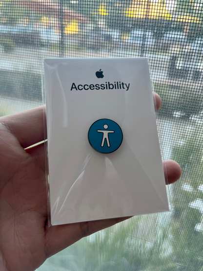 Hand holding a blue accessibility logo pin. Above says Apple accessibility.
