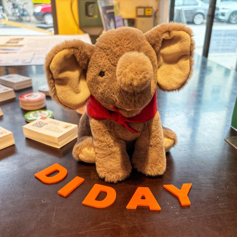 Unser Maskottchen hat ein rot-weißes Franken-Halstuch bekommen und sitzt auf einem Tisch, vor sich die Buchstaben „DIDAY“ und daneben Visitenkarten für unsere Signal-Gruppen. Im Hintergrund ist der Eingang des ZAM zu sehen.