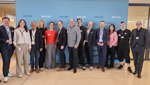 Vor einer Fotowand der CDU/CSU-Bundestagsfraktion stehen insgesamt 13 Personen und lächeln in die Kamera. In der Mitte der Gruppe steht der Bundestagsabgeordnete Henri Schmidt.